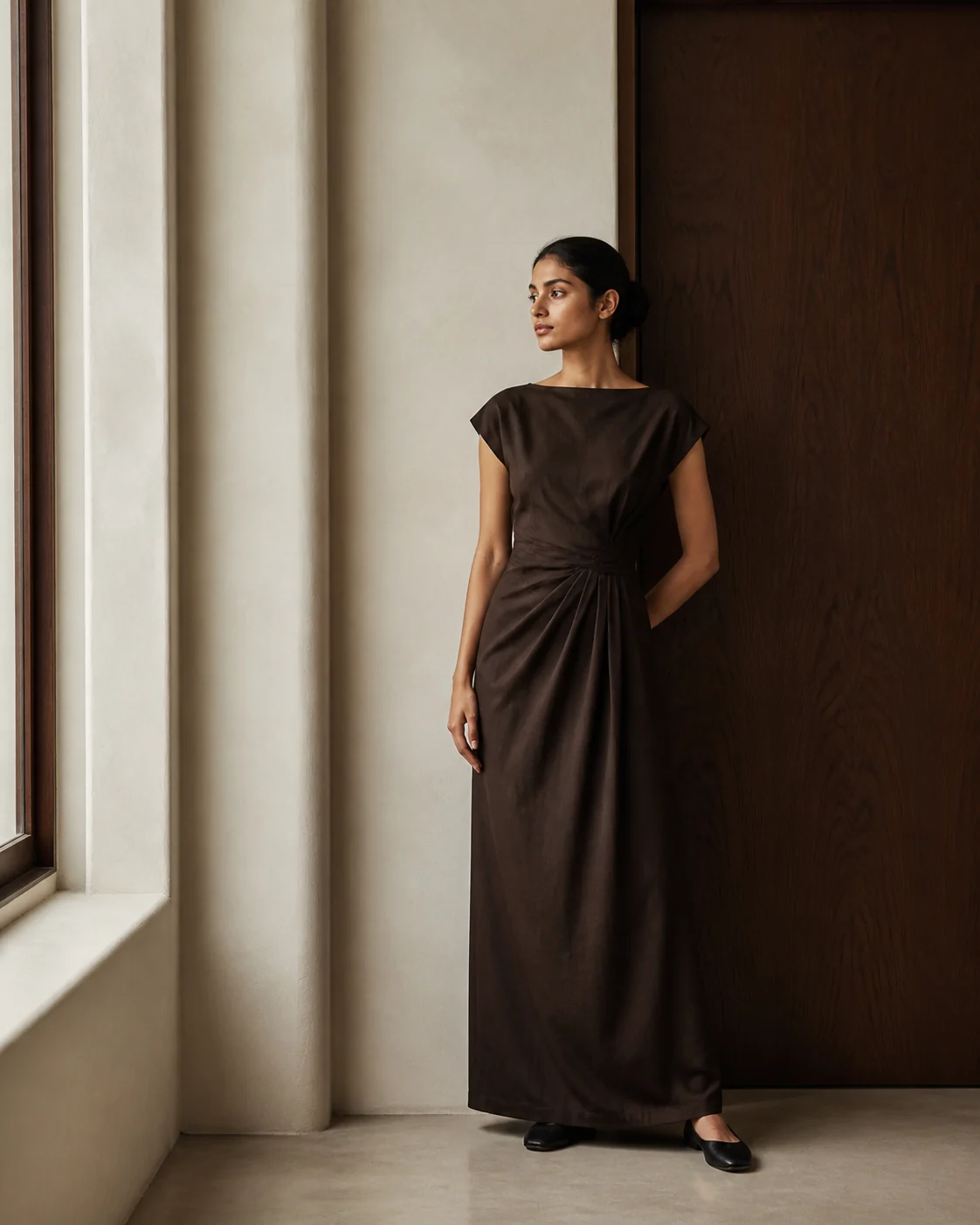 Woman wearing a deep espresso cotton dress beside ivory plaster and dark wood
